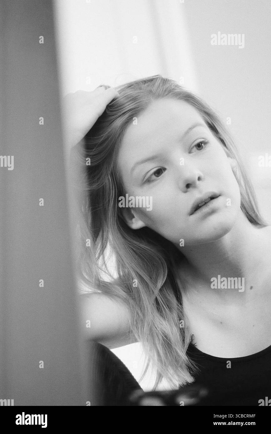 Jeune femme fixant ses cheveux devant un miroir en noir et blanc Banque D'Images