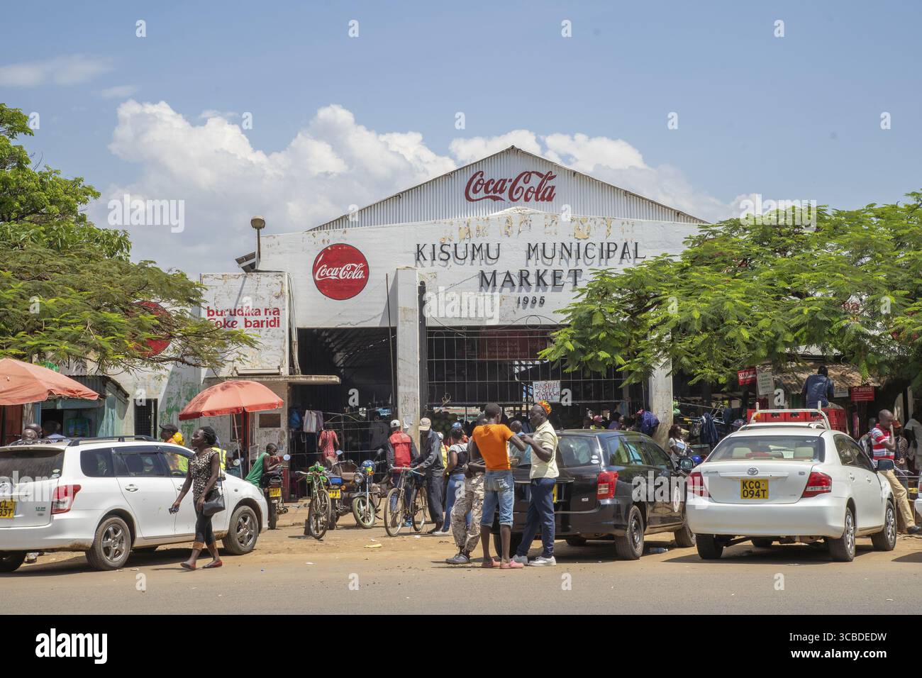 Kisumu, Kenya - 13 mai 2021 : vue sur le marché municipal animé de Kisumu sous un ciel lumineux, où la vie dynamique se déroule au milieu des voitures garées et des emblématiques panneaux Coca-Cola. Banque D'Images