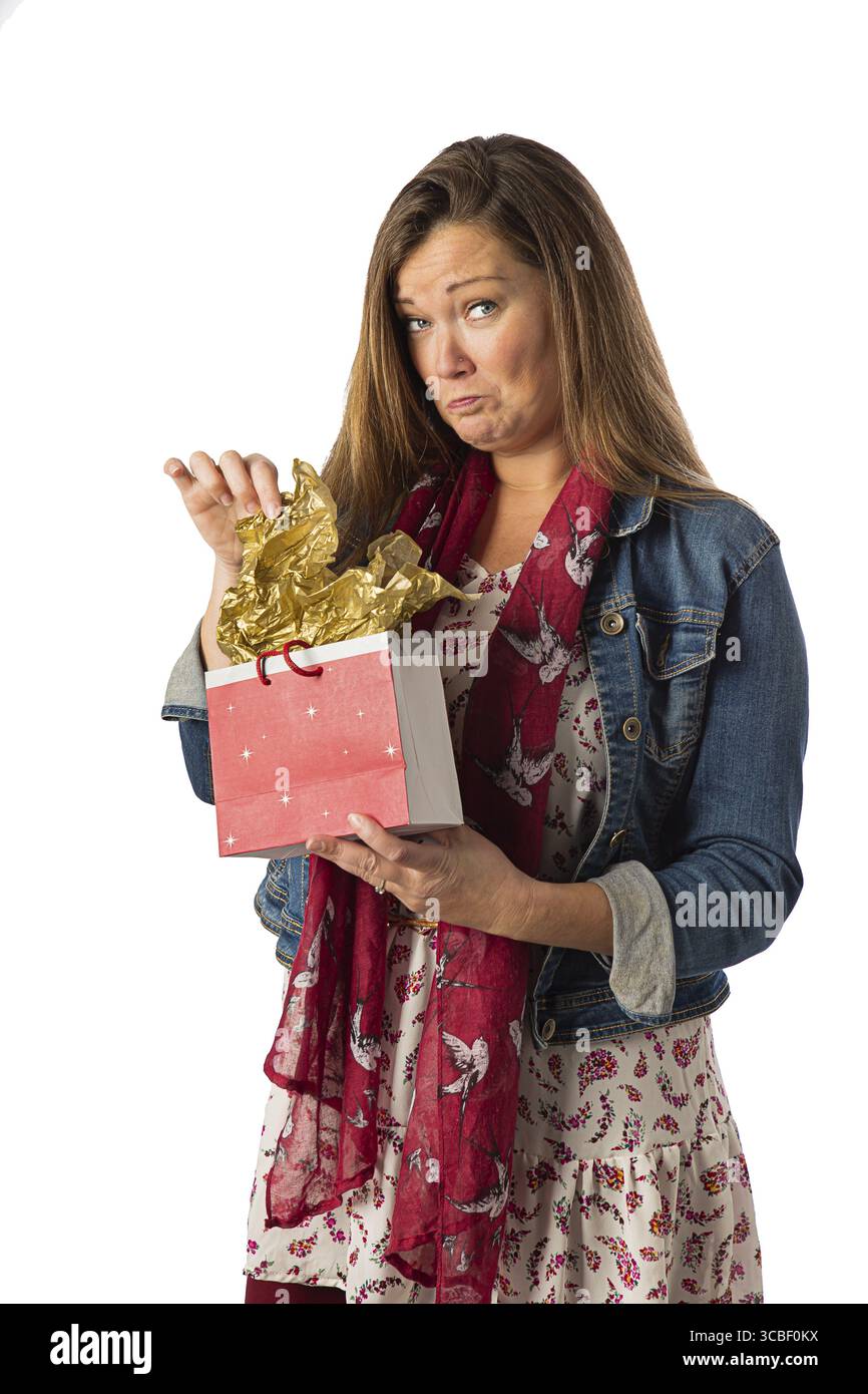 Femme de quarante ans, portant des vêtements de style bohème, ouvrant un sac cadeau, avec une expression malheureuse, isolée sur un fond blanc Banque D'Images