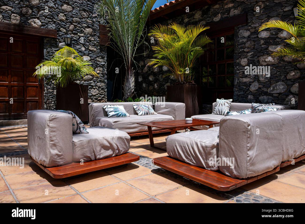 Un patio avec un grand canapé et plusieurs canapés plus petits. Le patio est entouré d'un mur de pierre et a une atmosphère tropicale Banque D'Images