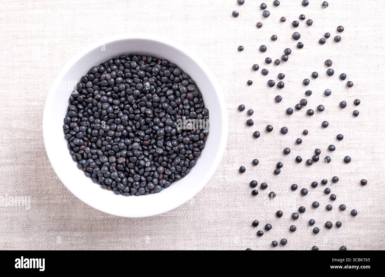 Lentilles béluga, lentilles noires, dans un bol en bois sur lin. Variété séchée de petites lentilles, Lens esculenta, également connue sous le nom de lentilles de caviar. Banque D'Images