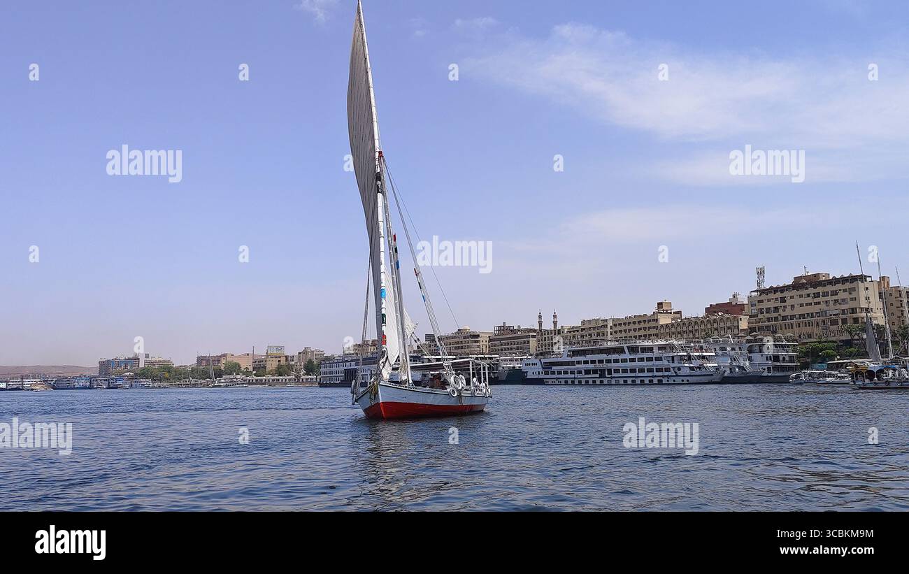 Felucca naviguant sur le nil à Assouan, Egypte, avec des bâtiments le long de la rive Banque D'Images