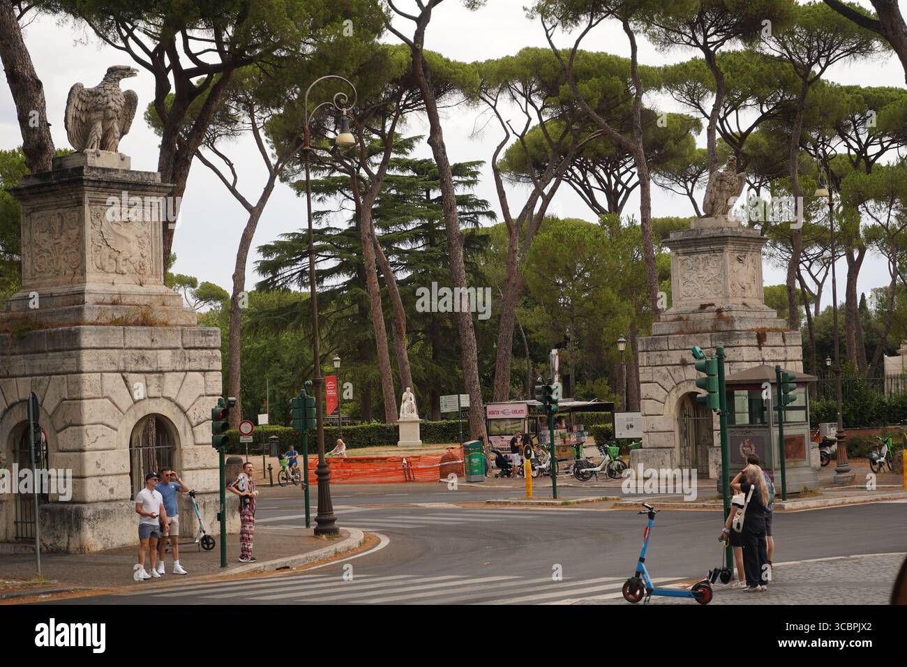 Deux grands piliers en pierre ornés avec des statues d'aigle sur le dessus se dressent à l'entrée d'un parc à Rome. Les gens sont visibles dans la rue. Banque D'Images