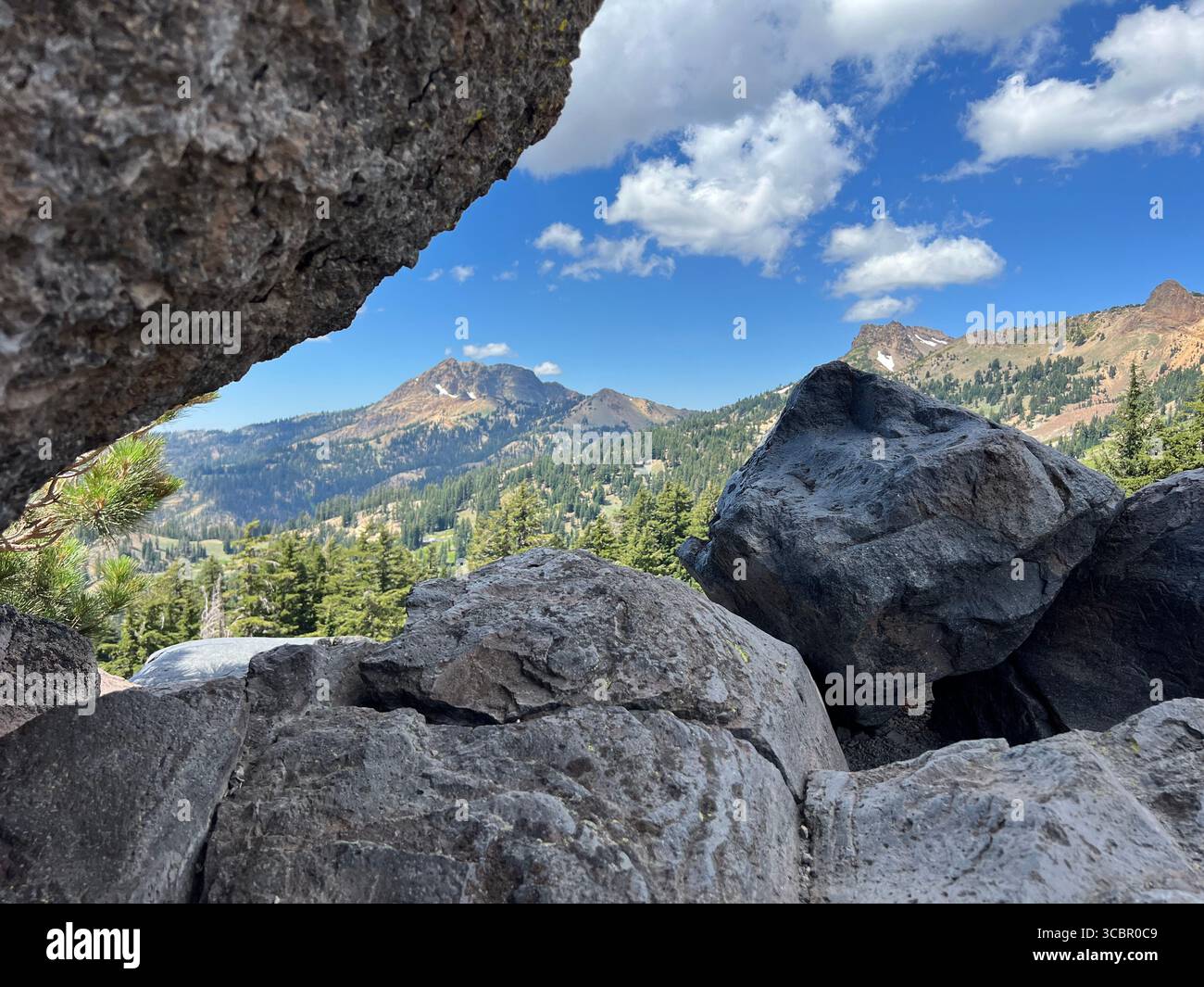Trois rochers uniques encadrent les pics et les forêts du parc national volcanique de Lassen, contrastant avec des roches sombres et accidentées avec un ciel lumineux et une nature sauvage vibrante. - Image de stock capturée avec un smartphone