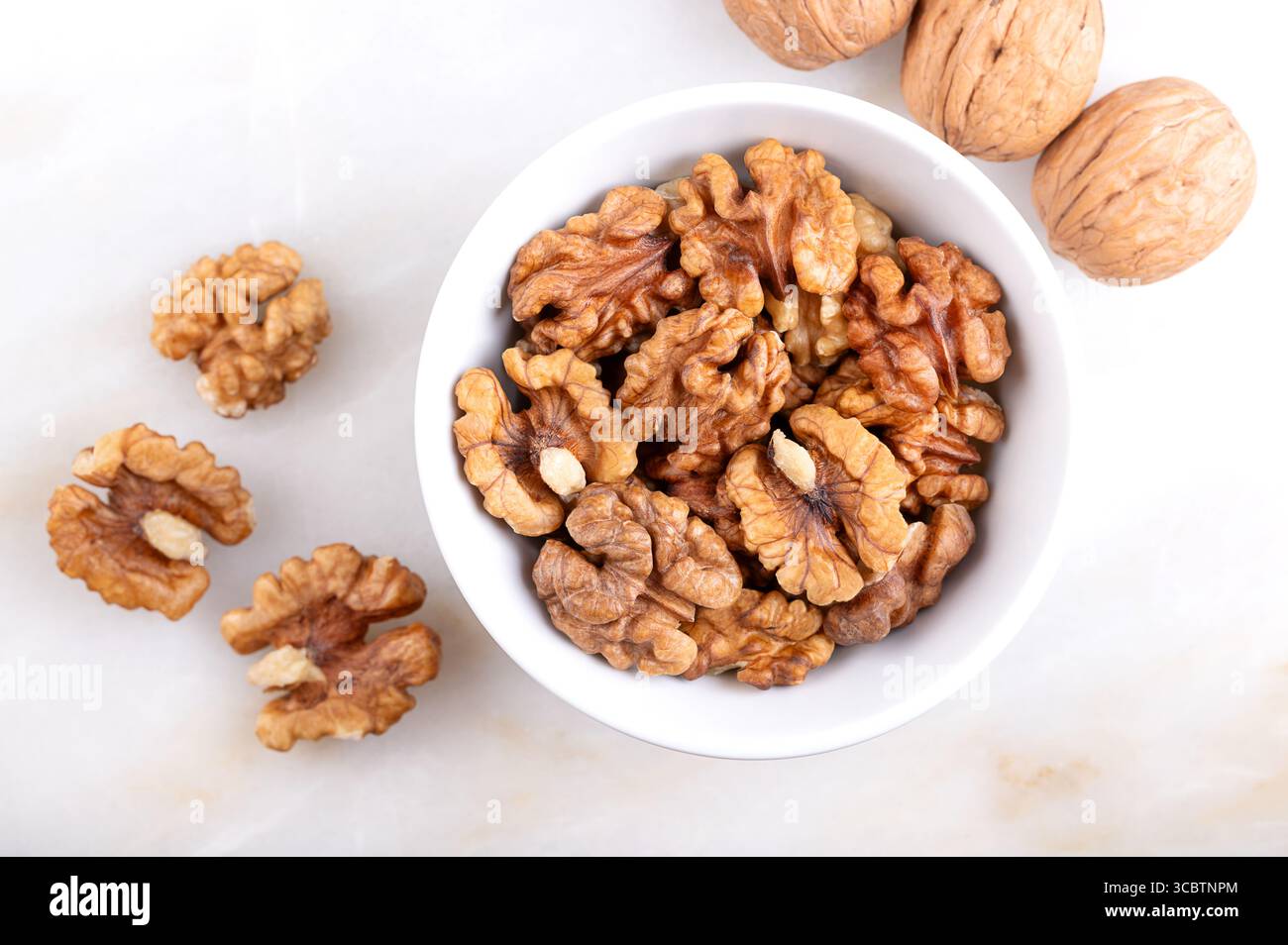 Moitiés de noyaux de noix, dans un bol blanc, sur une surface en marbre. Moitiés décortiquées et séchées de cerneaux de noix, graines de noyer commun, Juglans regia. Banque D'Images