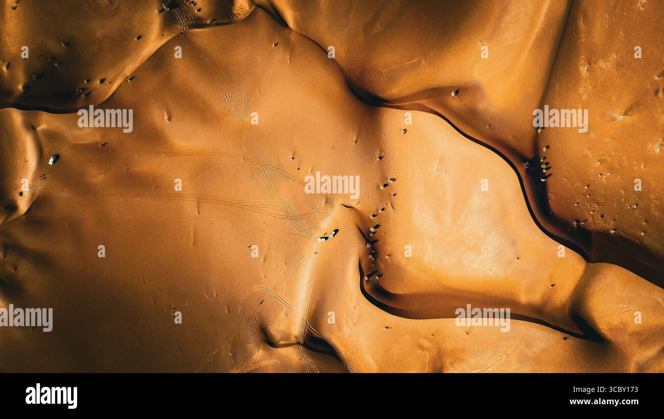 Vue aérienne de haut en bas des dunes de sable dans le désert de LUT (Kavir LUT), Iran—véhicules 4x4 et pistes courbées à travers des crêtes dorées en forme de vent. Banque D'Images
