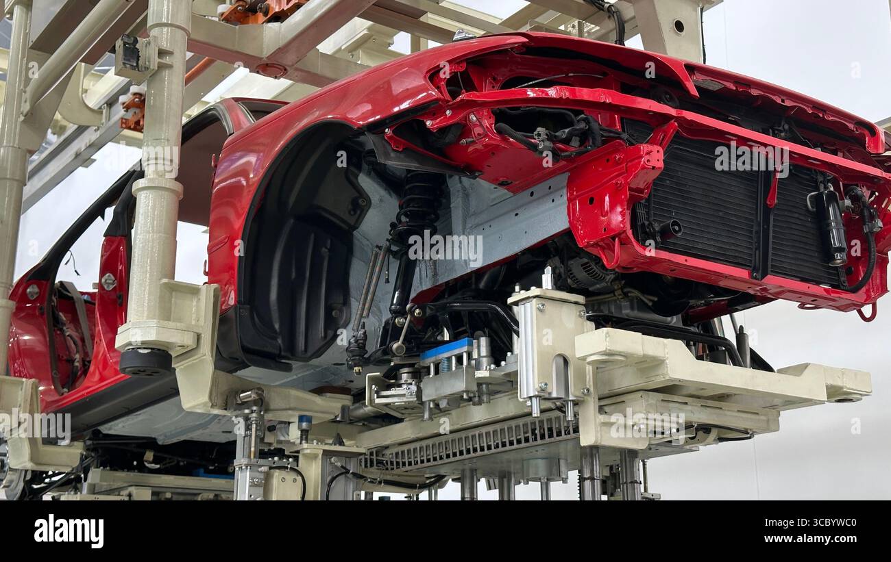 Un châssis de voiture rouge sur une chaîne de montage automatisée à l'intérieur d'une usine de fabrication moderne. Banque D'Images