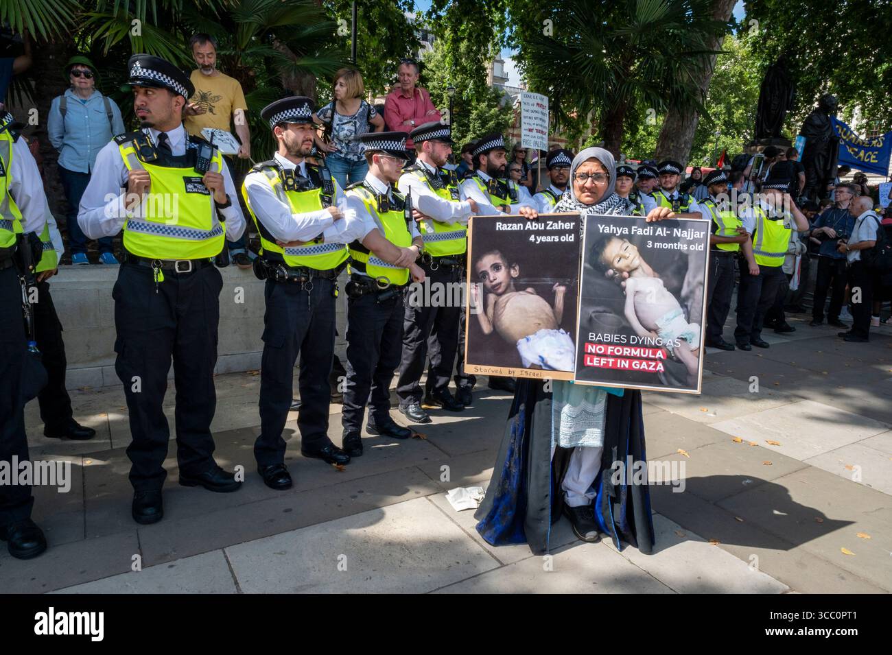 Une palestinienne avec des affiches d'enfants émaciés devant une rangée de policiers. Manifestation en soutien à Palestine action, Londres, 09/08/2025. Banque D'Images