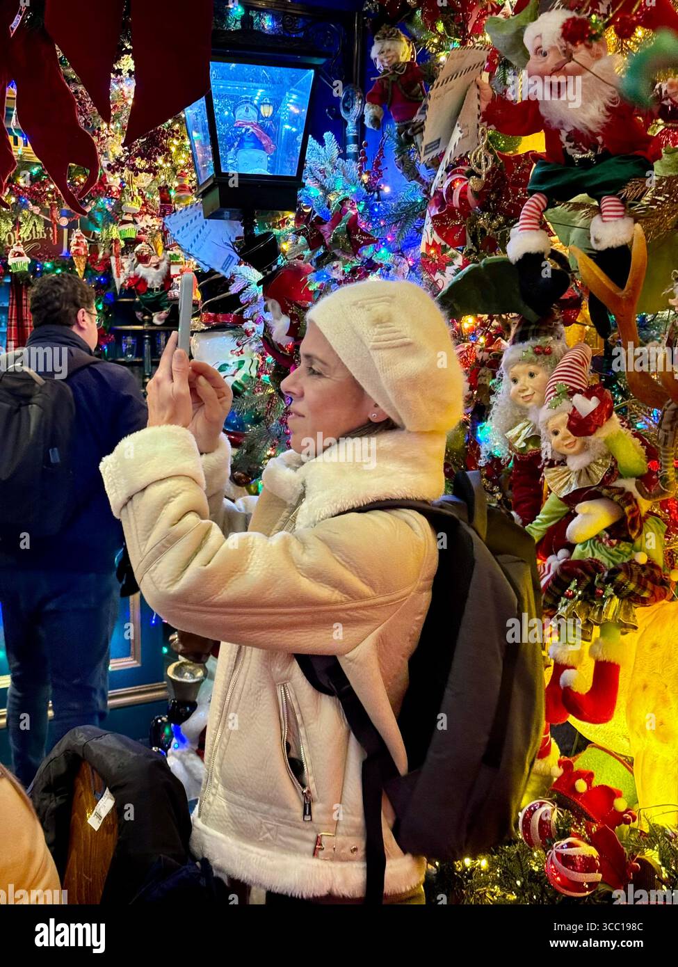 Touriste prenant des photos à l'intérieur du café 'Little Kook' à Athènes, décoré pour la période des fêtes de fin d'année avec des lumières de Noël vibrantes et des décorations festives. - Image de stock capturée avec un smartphone