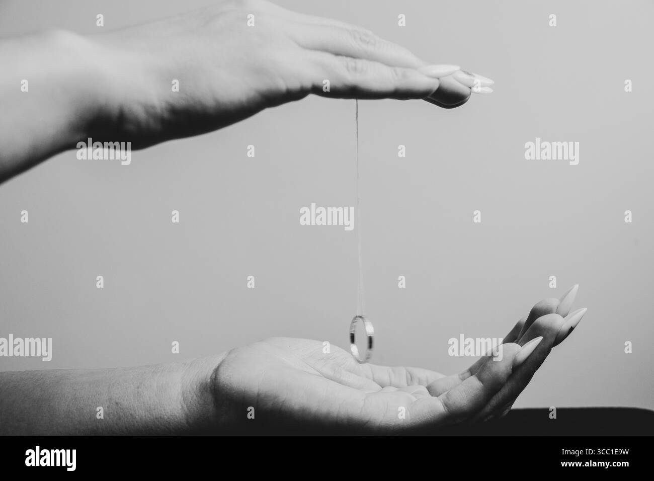 Rituel avec un anneau sur une ficelle entre les mains féminines, gros plan en noir et blanc Banque D'Images