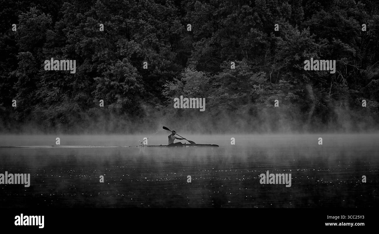 Photo en noir et blanc d'un kayak poussant sur une eau brumeuse Banque D'Images