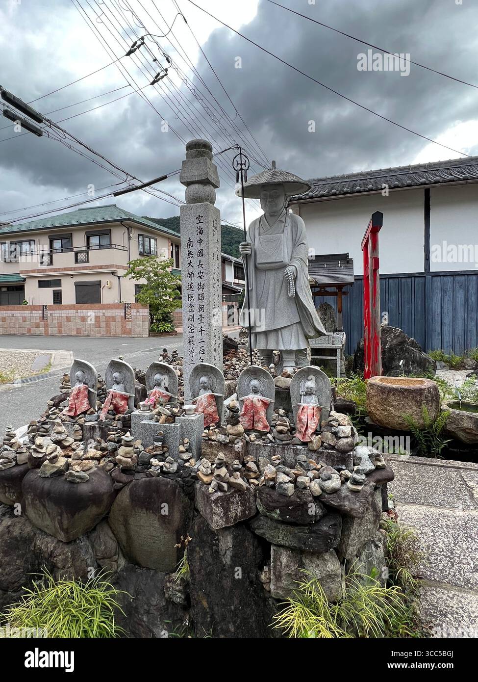 Statues bouddhistes et une statue de moine ornée d'offrandes de pierre dans un sanctuaire de quartier calme à Kyoto, au Japon. Banque D'Images