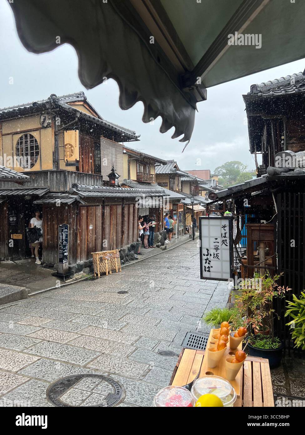 Scène de rue pluvieuse à Kyoto, au Japon, avec des bâtiments traditionnels en bois, des toits de tuiles et de la nourriture de rue exposés. Banque D'Images