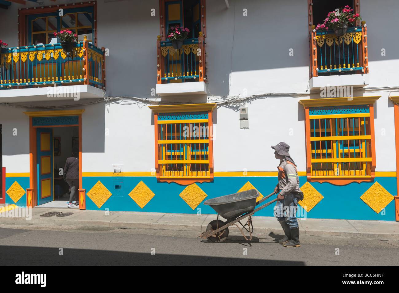Ouvrier poussant une brouette devant une maison aux couleurs vives à jardin, département d'Antioquia, Colombie Banque D'Images