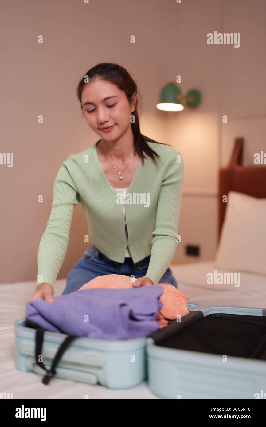 Femme asiatique adulte plie soigneusement les vêtements dans une valise sur un lit confortable organisant pour un voyage ou des vacances à venir Banque D'Images
