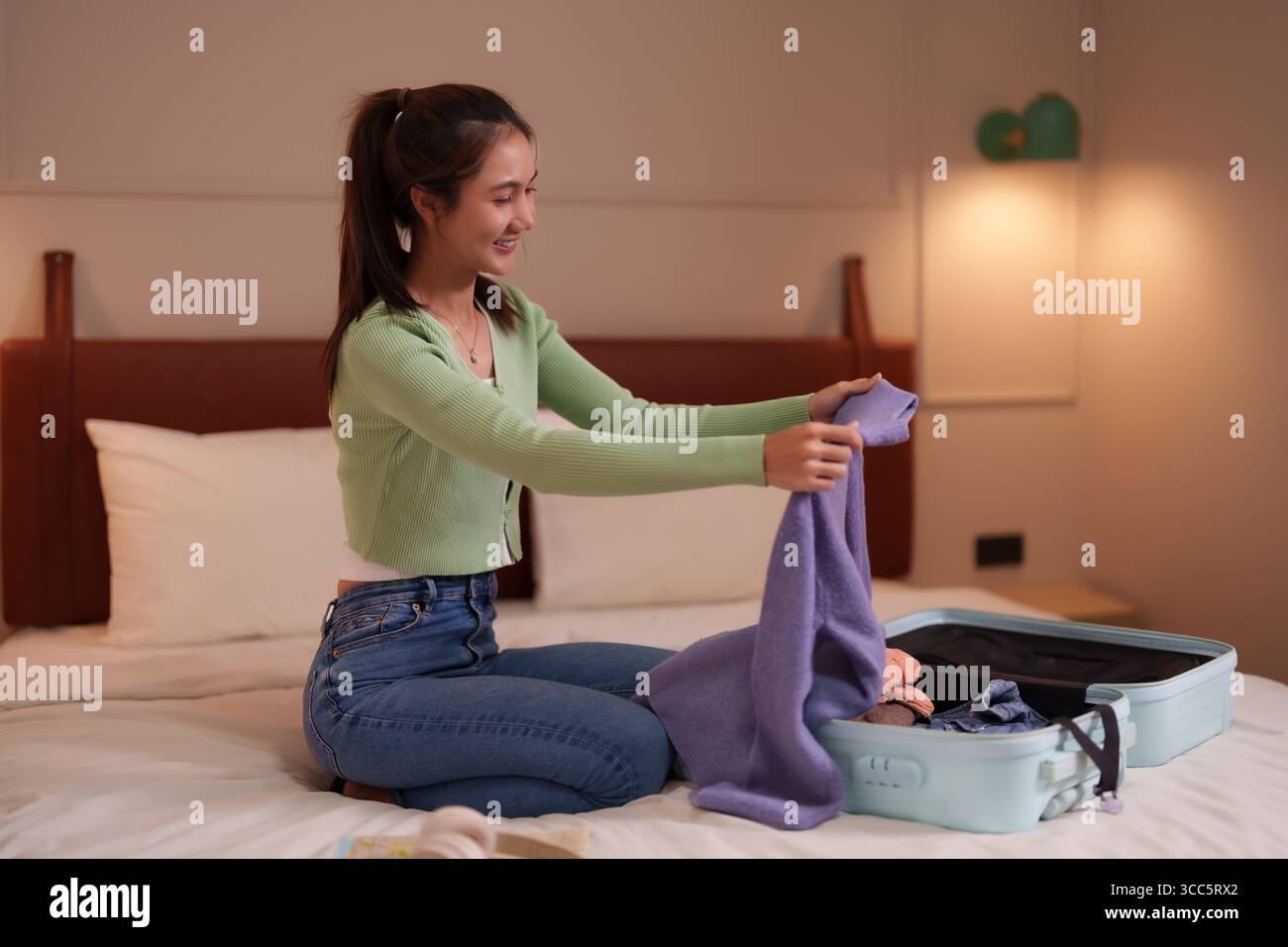 Jeune femme asiatique souriante pliant des vêtements organisant ses bagages pour des vacances ou un voyage d'affaires dans une chambre à coucher moderne planifier l'aventure à venir Banque D'Images