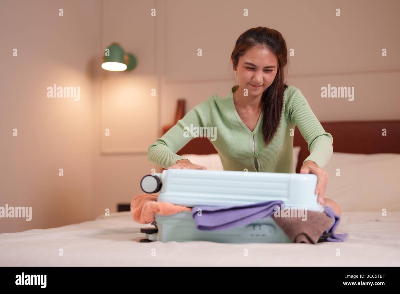 Les femmes asiatiques adultes luttent pour emballer une valise trop pleine sur un lit confortable se préparant à un voyage difficile à venir Banque D'Images
