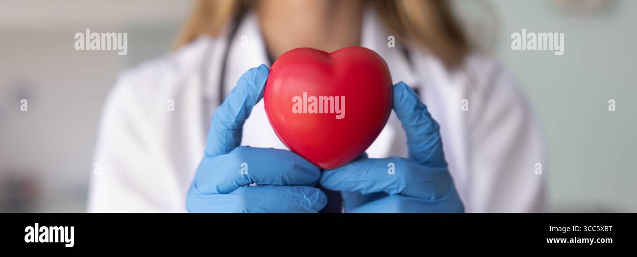 Mains d'un médecin cardio féminin dans des gants tenant le coeur rouge Banque D'Images
