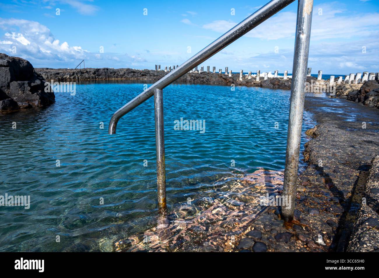 Une balustrade métallique est au-dessus d'un bassin d'eau. La rampe est rouillée et l'eau est claire Banque D'Images