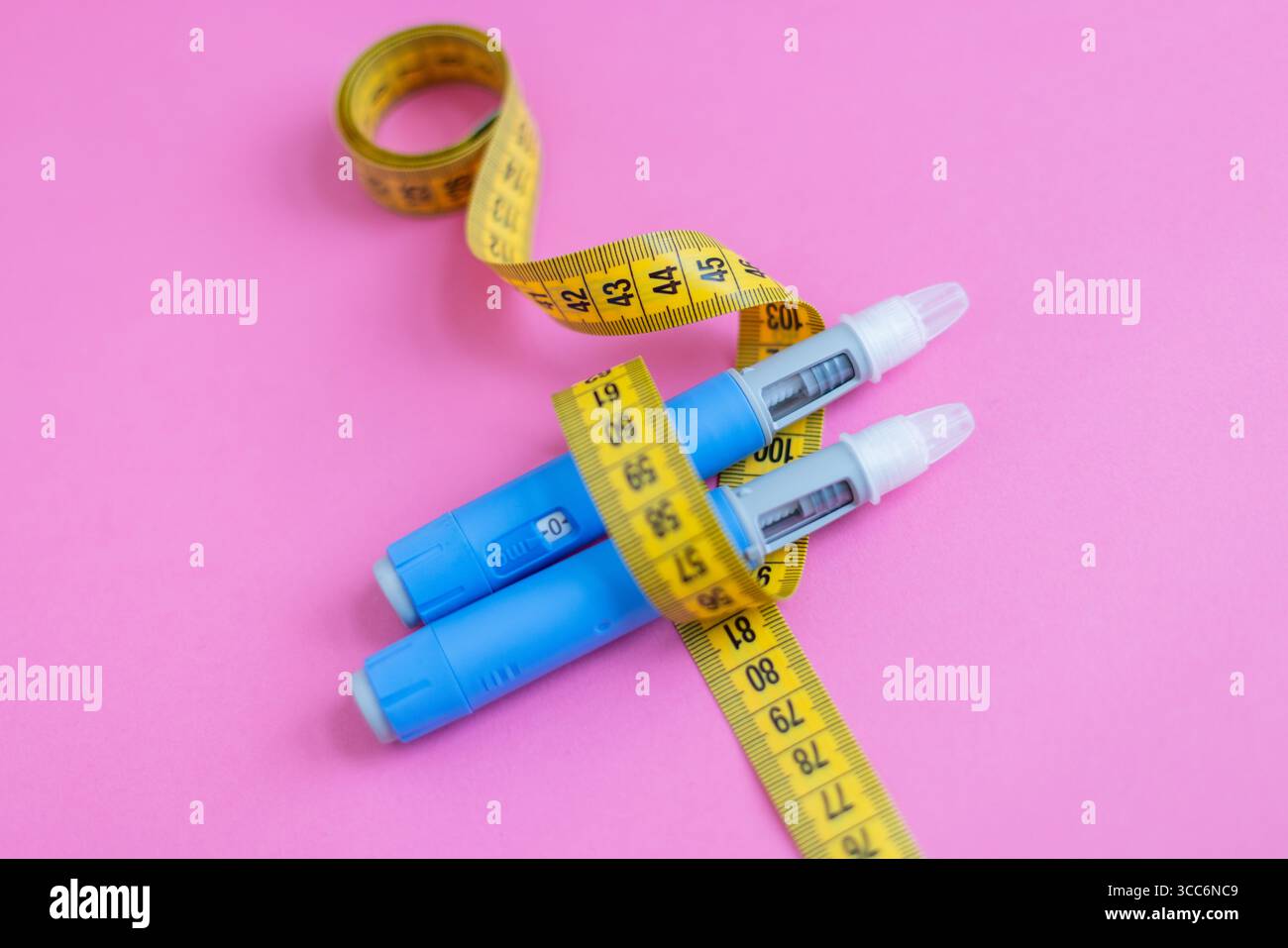 Perte de poids et concept d'insulinothérapie. Stylos à injection bleus et ruban à mesurer jaune disposés de manière créative sur fond rose. Injection de drogues Ozempic Banque D'Images