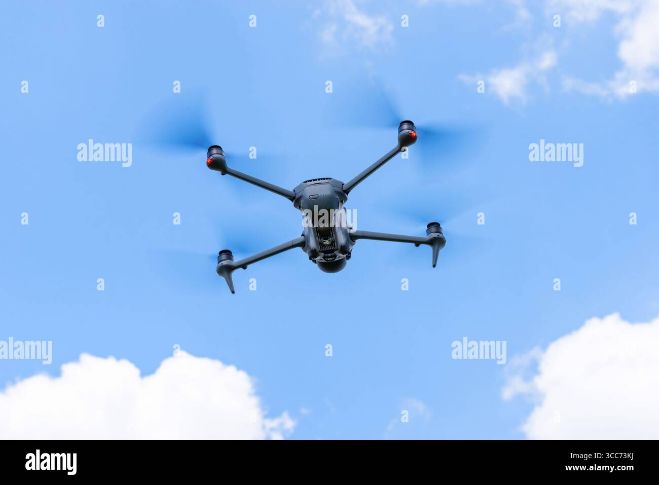 Vue de dessous d'un drone volant avec hélices tournantes contre ciel bleu et nuages Banque D'Images