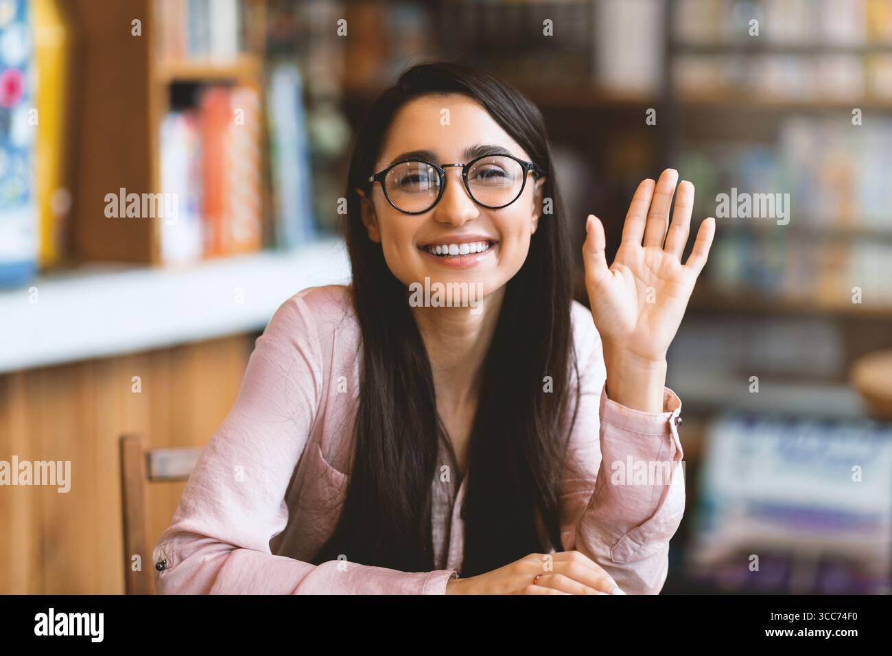 Appel vidéo. Heureuse jeune femme arabe saluant quelqu'un, ayant une conférence virtuelle, agitant de la main à la caméra et souriant Banque D'Images