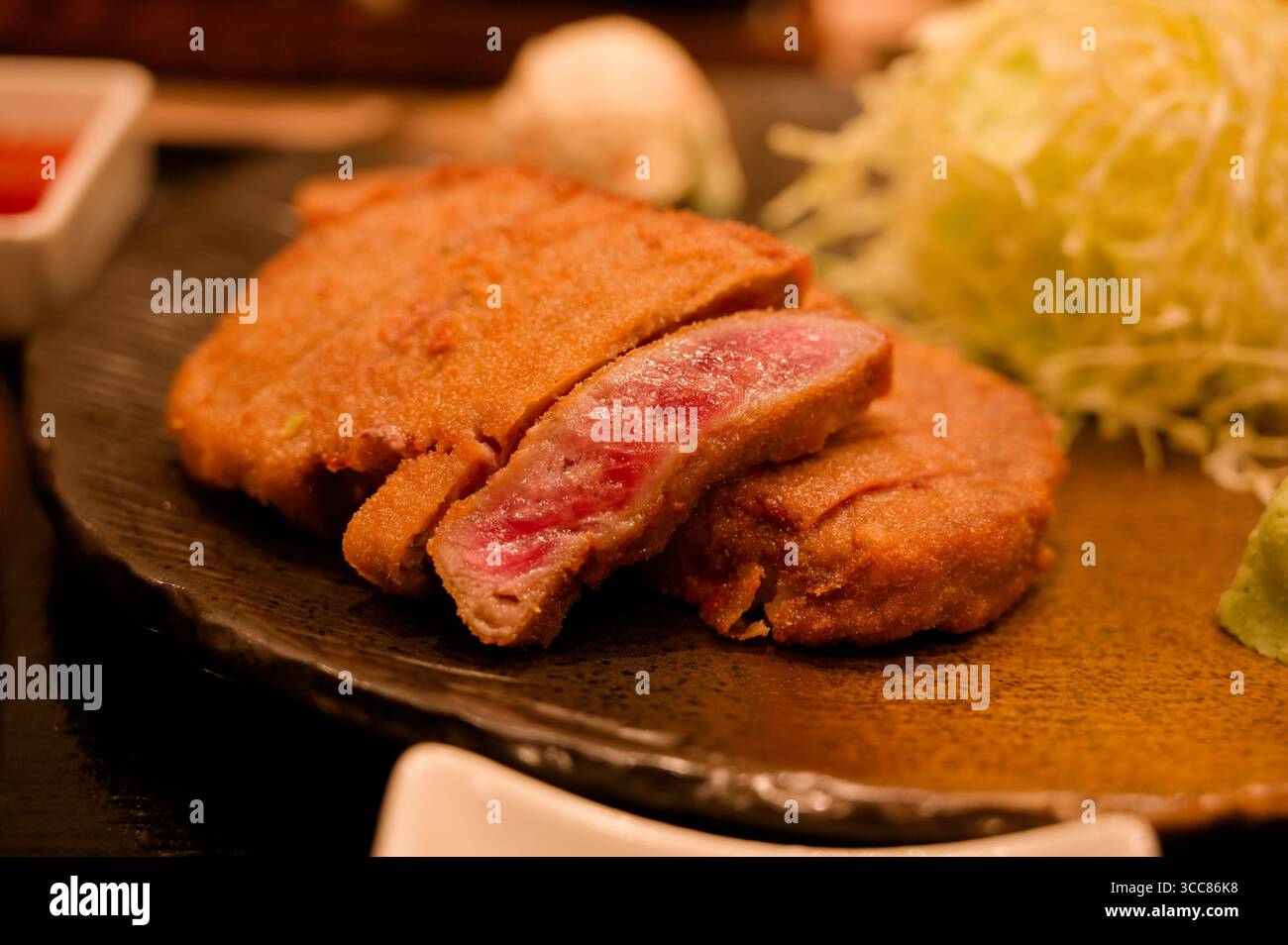 Gros plan du gyukatsu fraîchement cuit, côtelette de bœuf panée japonaise, servi avec du chou râpé sur une assiette traditionnelle en céramique Banque D'Images