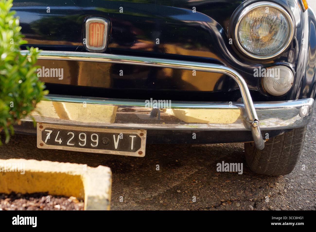 Gros plan de la plaque de régionalisation, du pare-chocs et de l'écusson d'une Fiat 500 classique noire à la lumière dorée. Montefiascone, région du Latium, Italie. 11 juin 2025. Banque D'Images