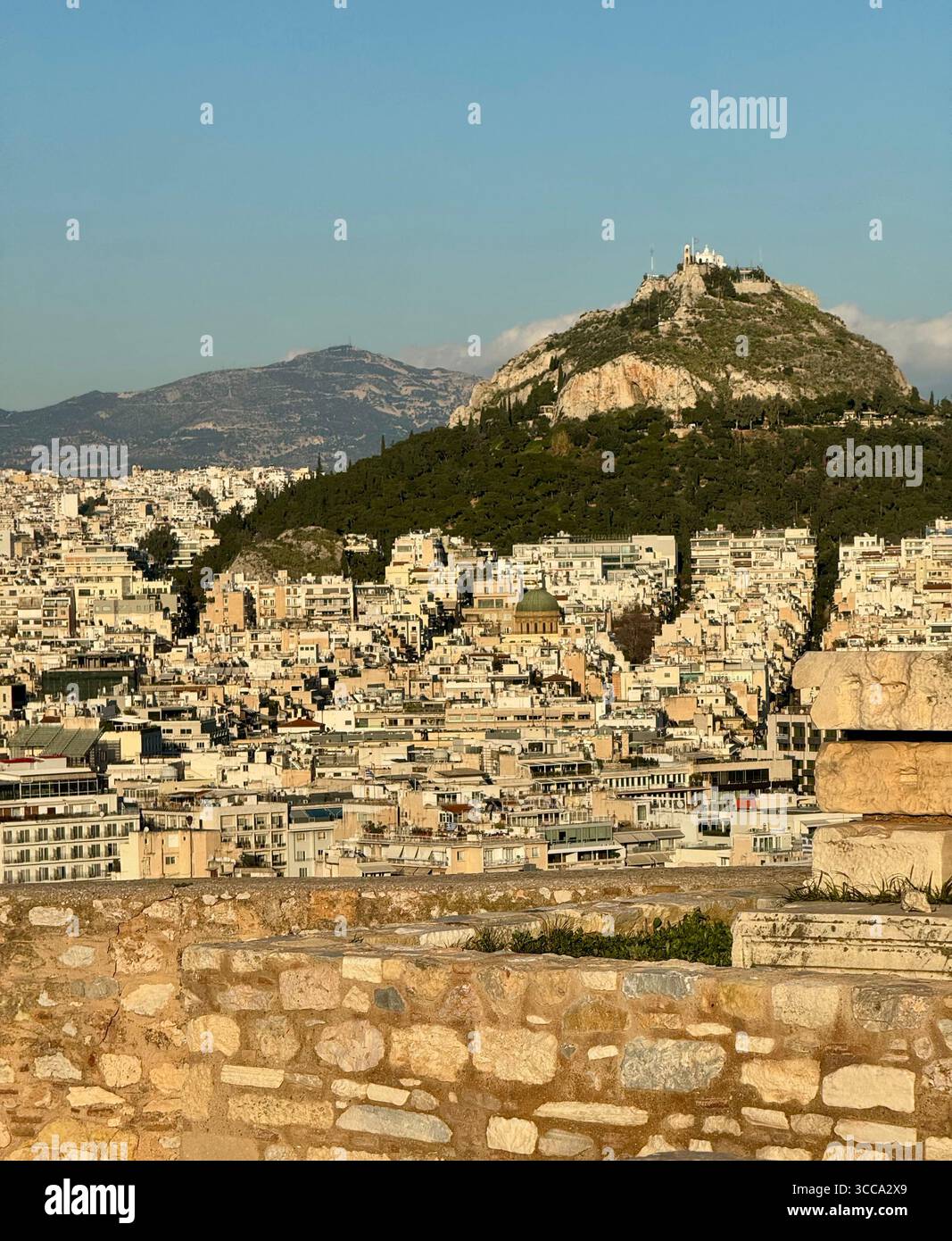 Vue panoramique de la montagne Lycabette s'élevant au-dessus du paysage urbain dense d'Athènes, vu du point de vue de l'Acropole. - Image de stock capturée avec un smartphone
