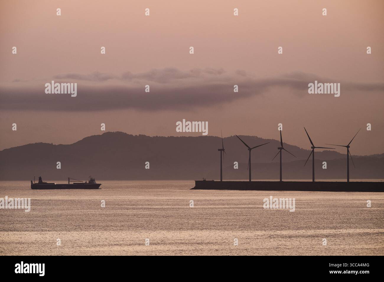 Cargo naviguant près d'un parc éolien offshore à l'aube, situé dans le port de bilbao, en espagne, symbolisant la coexistence du transport maritime et renouvelable Banque D'Images