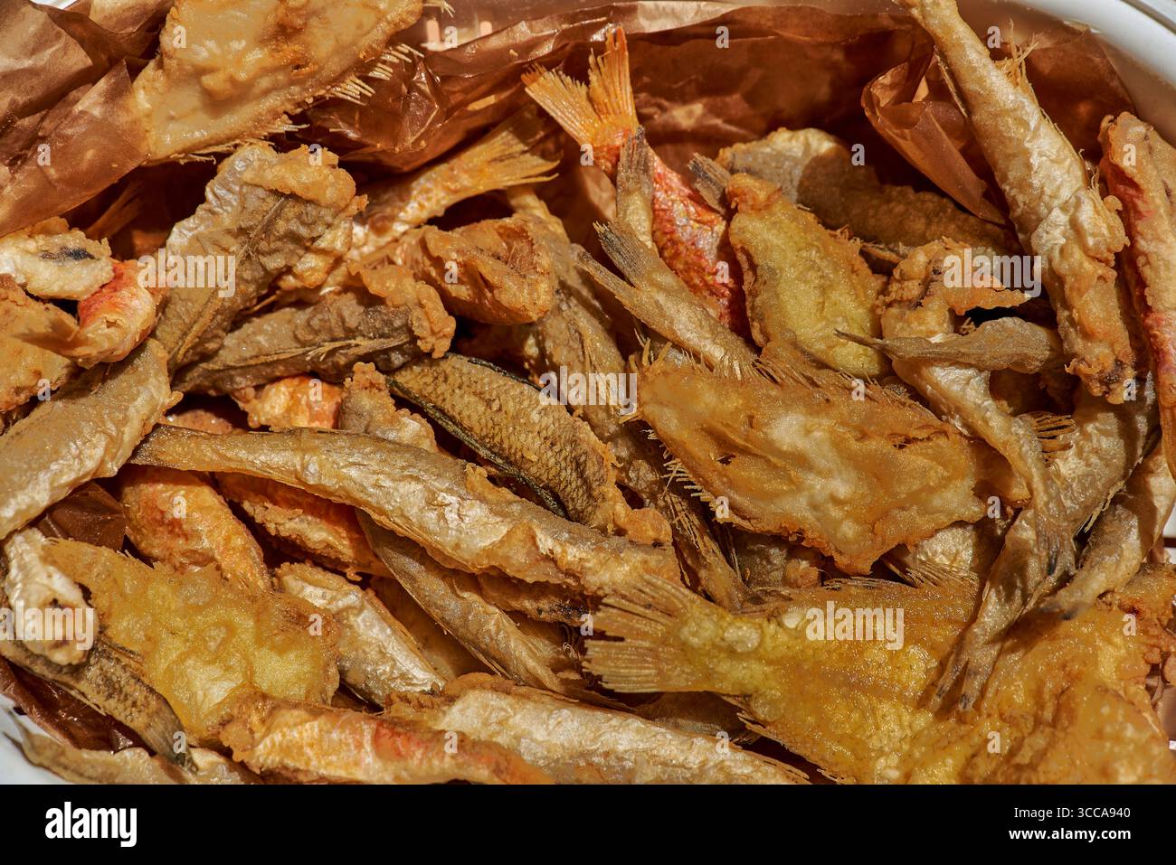 Un mélange de petits poissons frits dorés se trouve sur du papier brun, leur revêtement croquant et texturé et des formes variées reflétant les fruits de mer rustiques du sud de l'Italie Banque D'Images