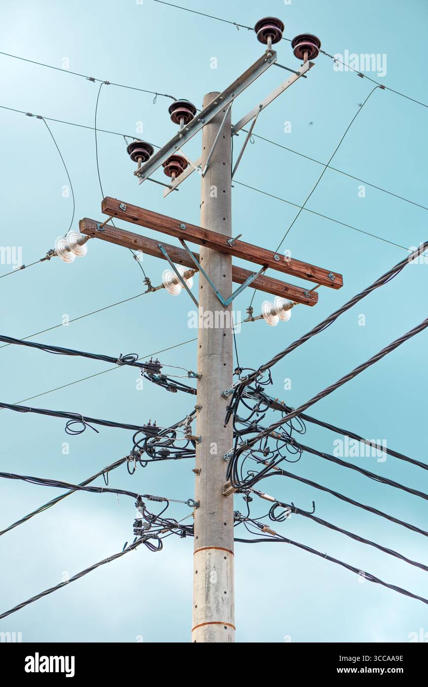Poteau utilitaire en béton avec des fils électriques et des isolants enchevêtrés contre un ciel bleu clair. Mise au point sélective. Banque D'Images