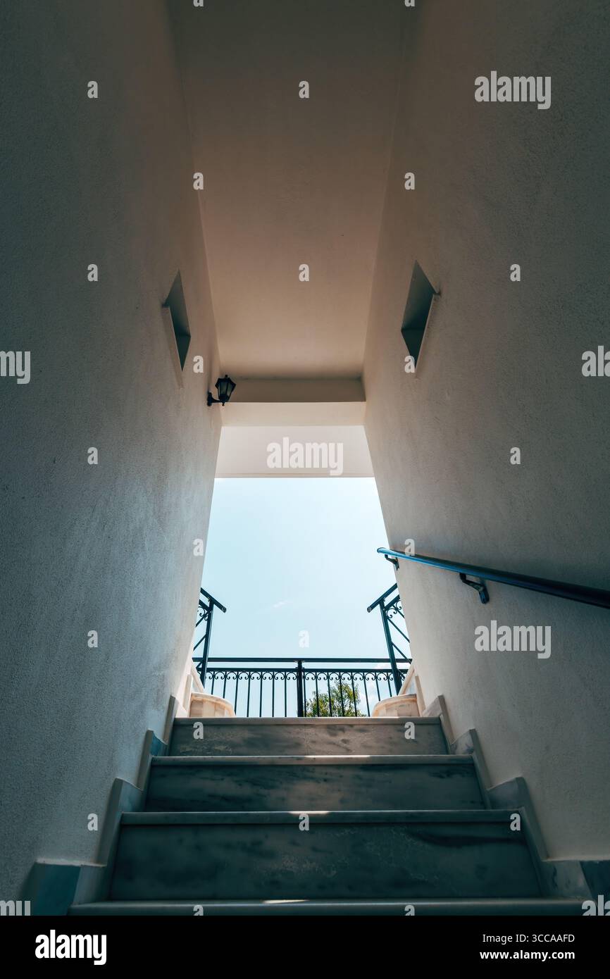 Vue en bas angle des escaliers en marbre menant à un ciel ouvert, encadrés par des murs blancs et des balustrades noires. Design architectural minimaliste avec lumière naturelle a Banque D'Images