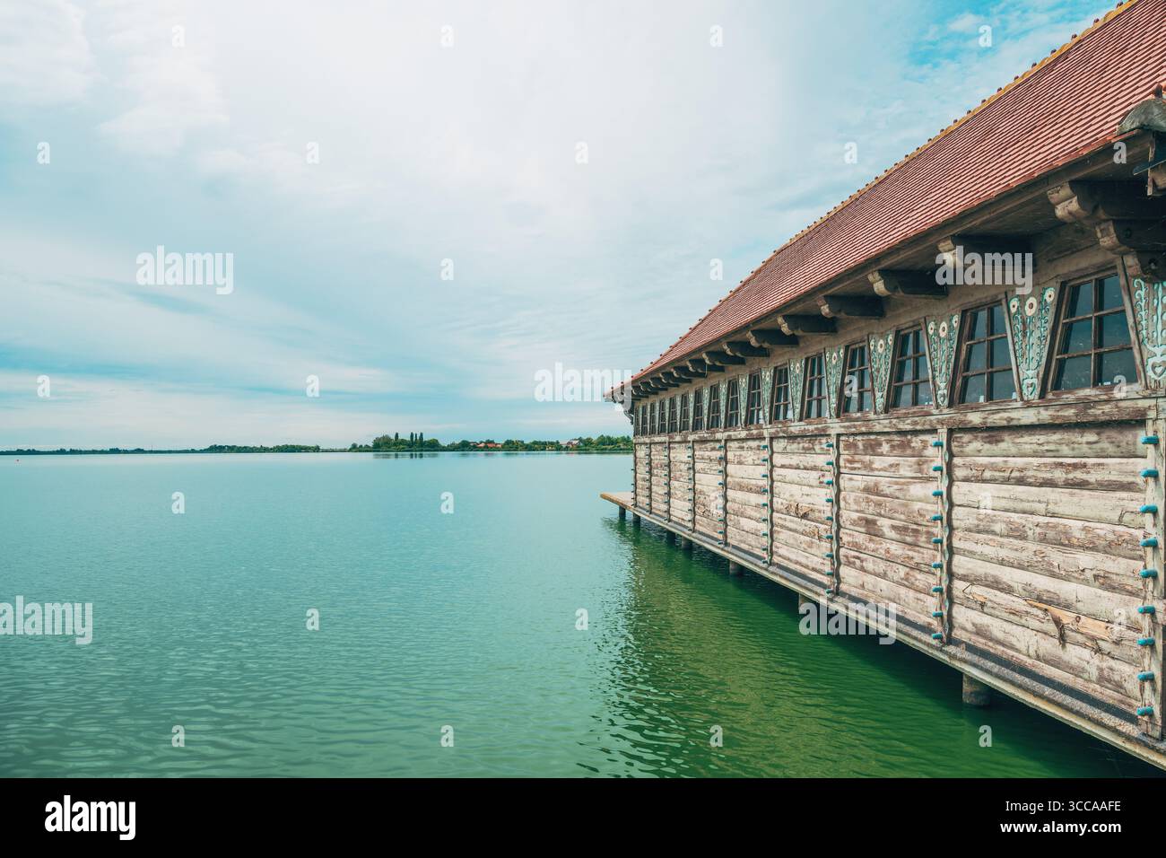 Hangar à bateaux traditionnel en bois avec des détails ornés sur le lac Palic, Serbie, s'étendant au-dessus de l'eau verte calme sous un ciel d'été lumineux. Mise au point sélective Banque D'Images