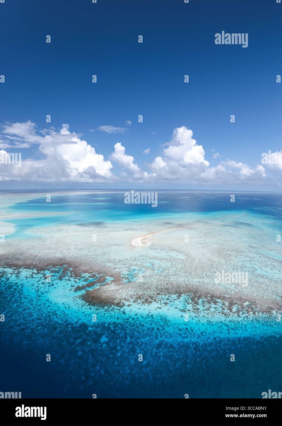 Vue aérienne des eaux turquoises vives tourbillonnant autour des récifs coralliens pâles sous un ciel lumineux avec des nuages moelleux, Fakarava, Iles Tuamotu-Gambier, Polynésie française. Banque D'Images