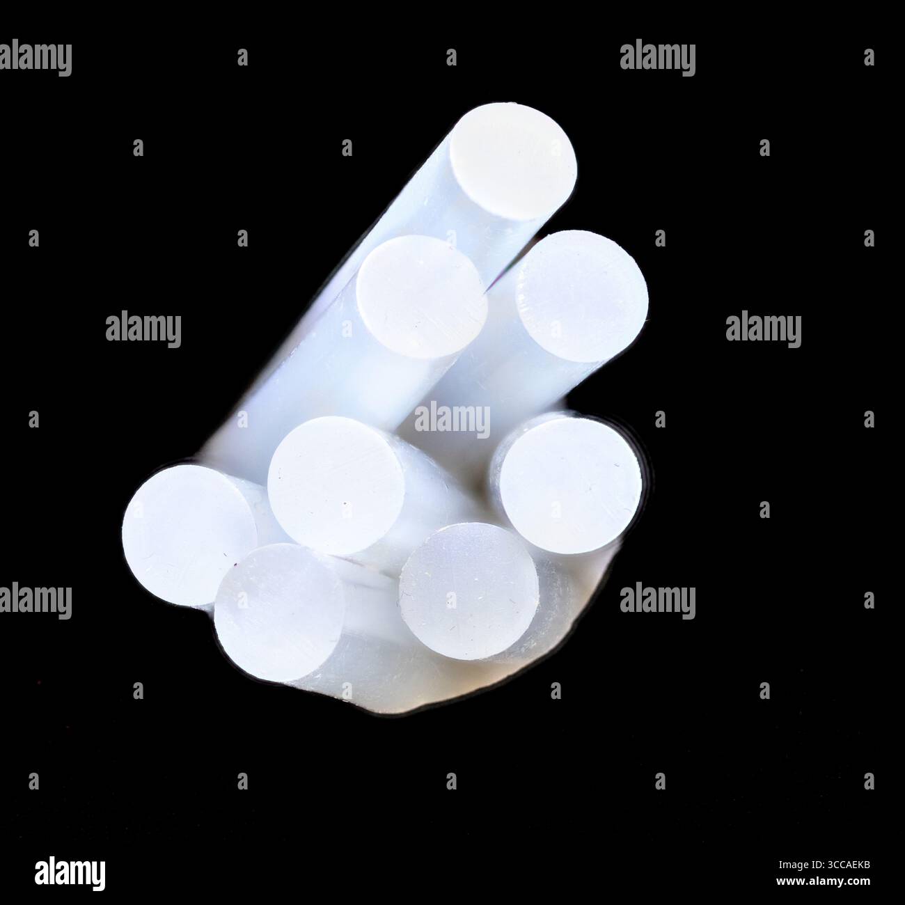 Plusieurs bâtons de colle chaude sont disposés en forme de pyramide sur un fond sombre, créant un contraste visuel intéressant Banque D'Images