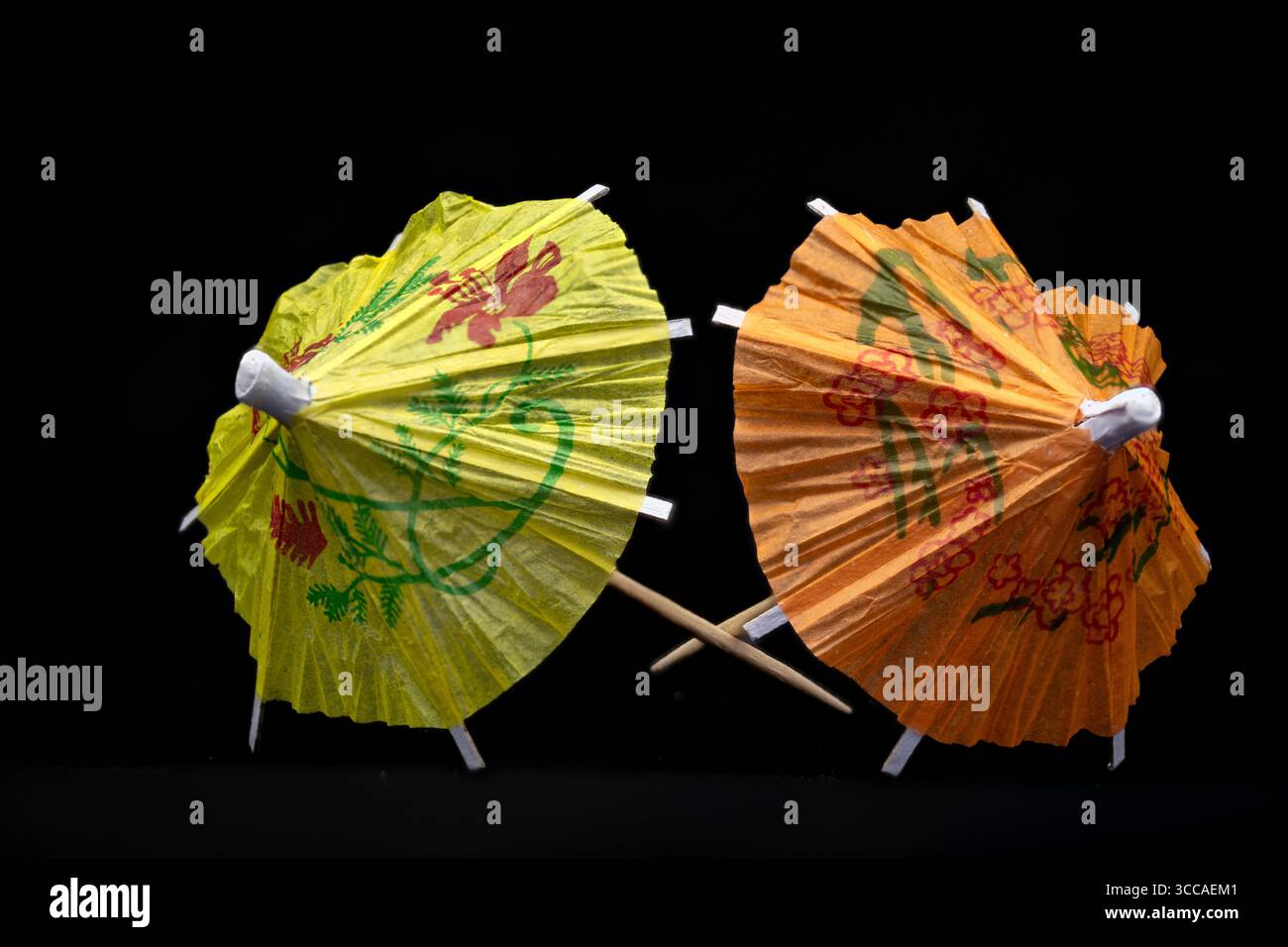 Deux parapluies cocktail colorés avec des décorations florales se croisant sur un fond noir, ajoutant une touche d'élégance tropicale Banque D'Images