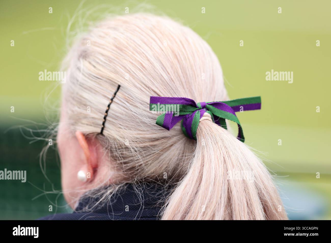 Femme âgée portant un arc de cheveux aux couleurs de Wimbledon assis sur l'un des courts extérieurs aux championnats de Wimbledon 2025, Londres, Angleterre, Royaume-Uni. Banque D'Images
