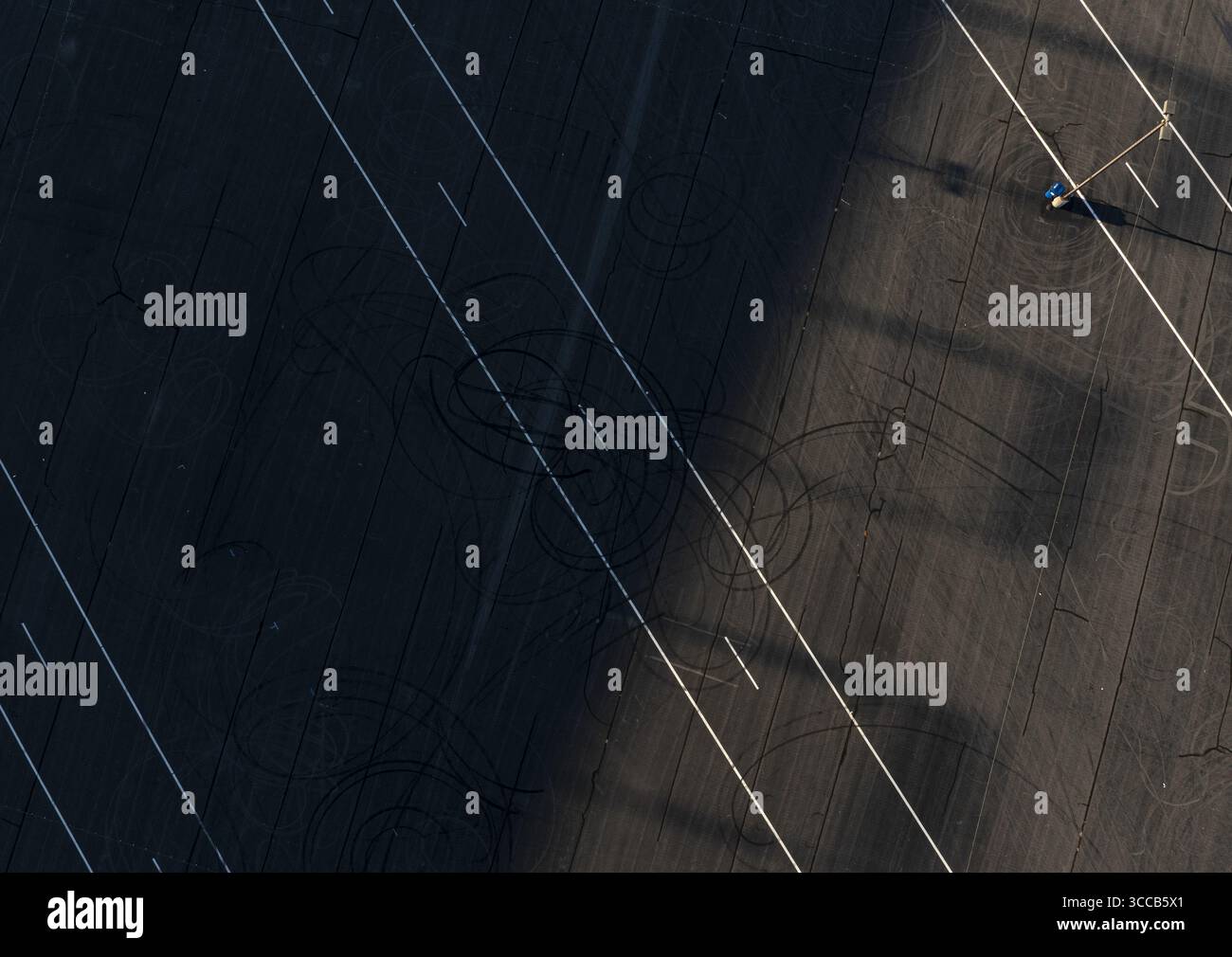 Concord, États-Unis - 28 juillet 2025 : vue aérienne du paysage asphalté dur, gravé avec des lignes pâles et les traînées fantomatiques de pneus, coupé en deux par une ombre dramatique. Banque D'Images