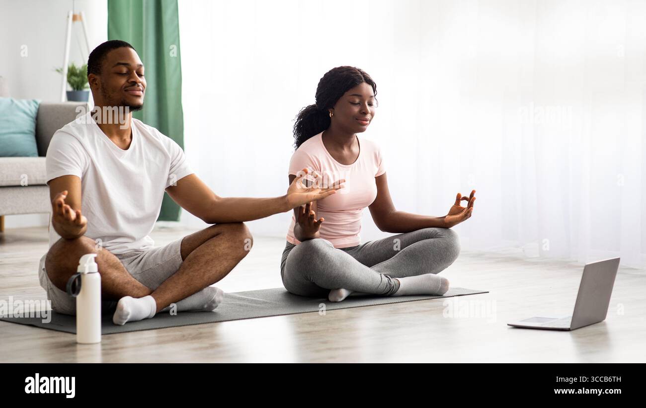 Paisible couple noir méditant à la maison, à l'aide d'un ordinateur portable Banque D'Images