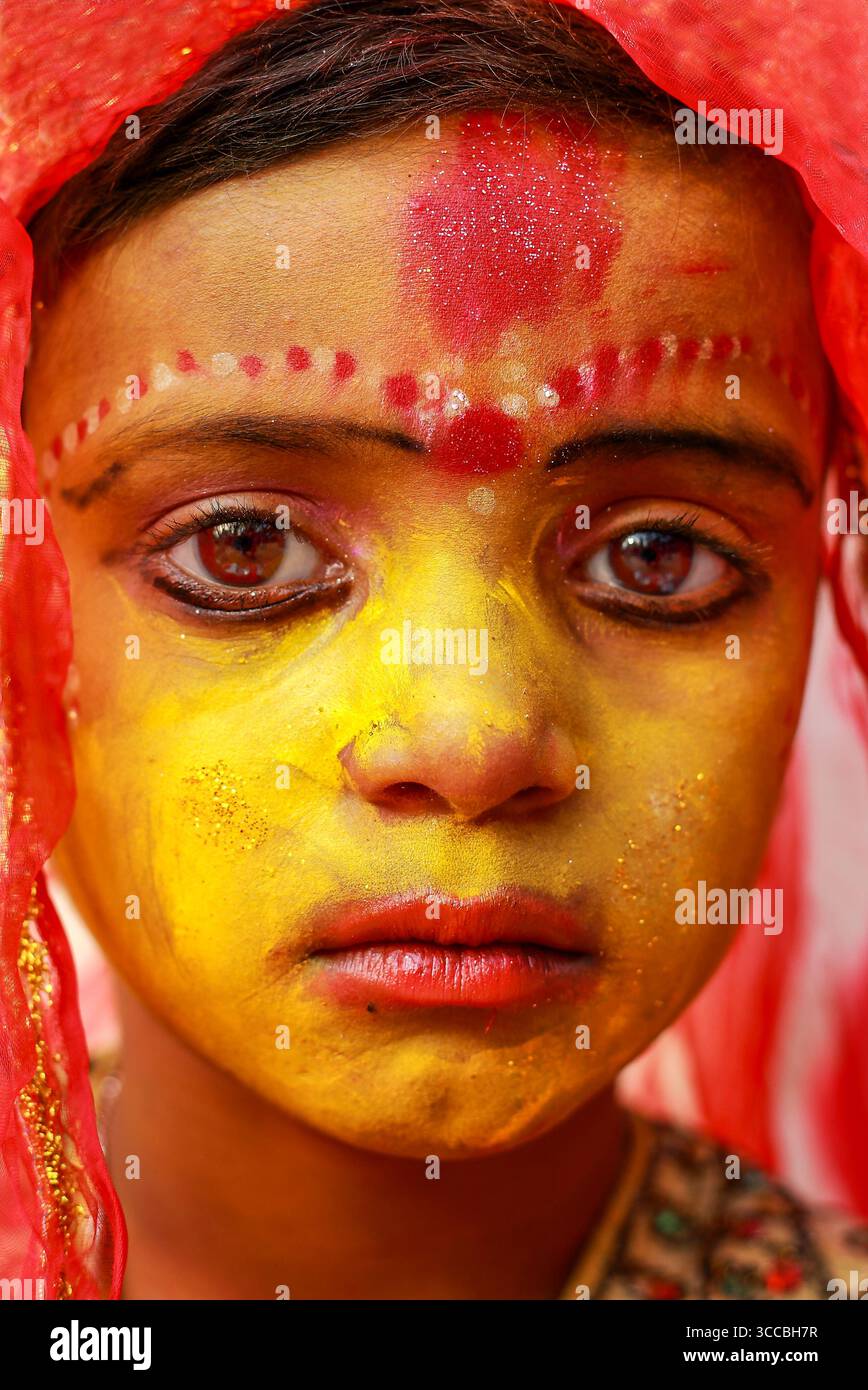 Colline de Chandanath, Bangladesh - 12 mars 2021 : vue d'une jeune fille peinte de jaune et rouge vif, ses yeux sombres tenant un regard solennel, encadrés par un délicat foulard rouge. Banque D'Images