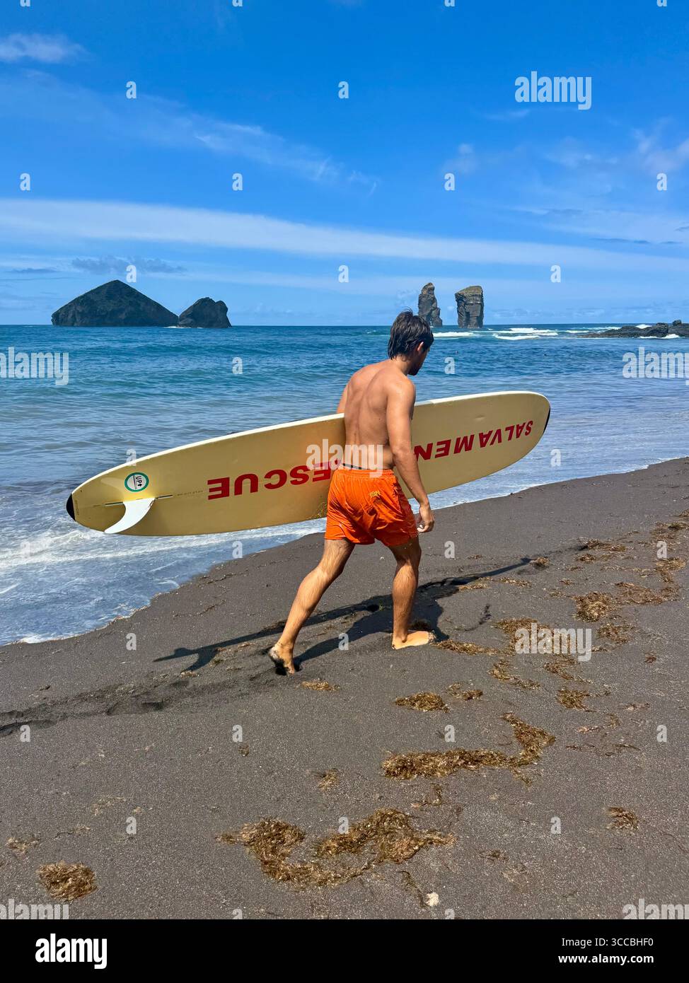 Sauveteur en service à Mosteiros Beach, île de São Miguel, Açores, Portugal, marchant sur le sable avec une planche de sauvetage. - Image de stock capturée avec un smartphone