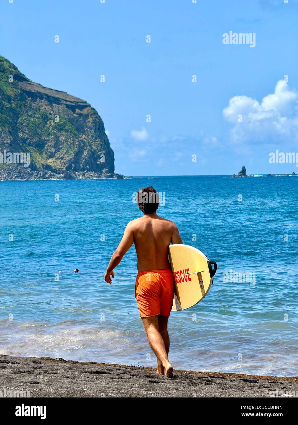Sauveteur en service à Mosteiros Beach, île de São Miguel, Açores, Portugal, marchant sur le sable avec une planche de sauvetage. - Image de stock capturée avec un smartphone