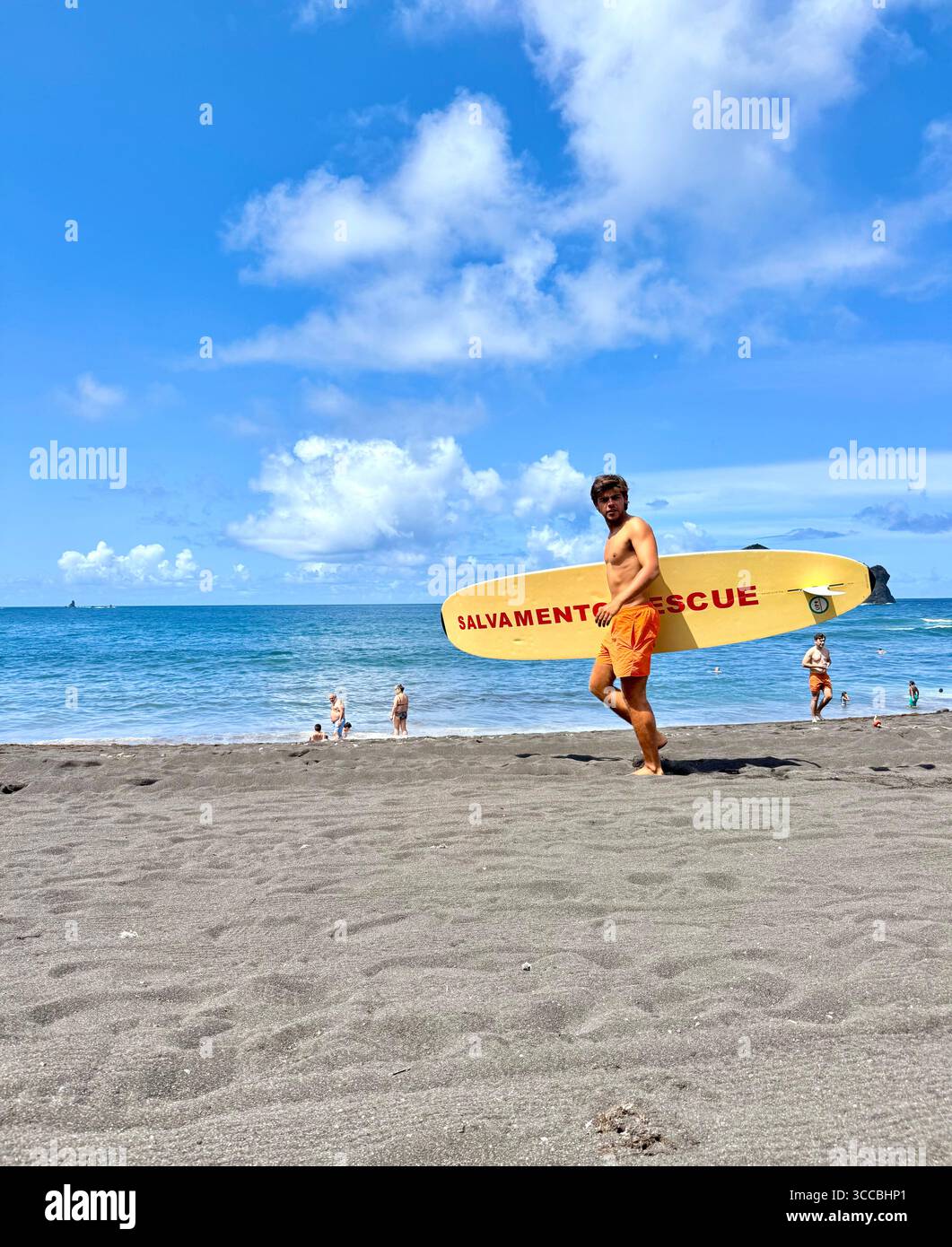 Sauveteur en service à Mosteiros Beach, île de São Miguel, Açores, Portugal, marchant sur le sable avec une planche de sauvetage. - Image de stock capturée avec un smartphone