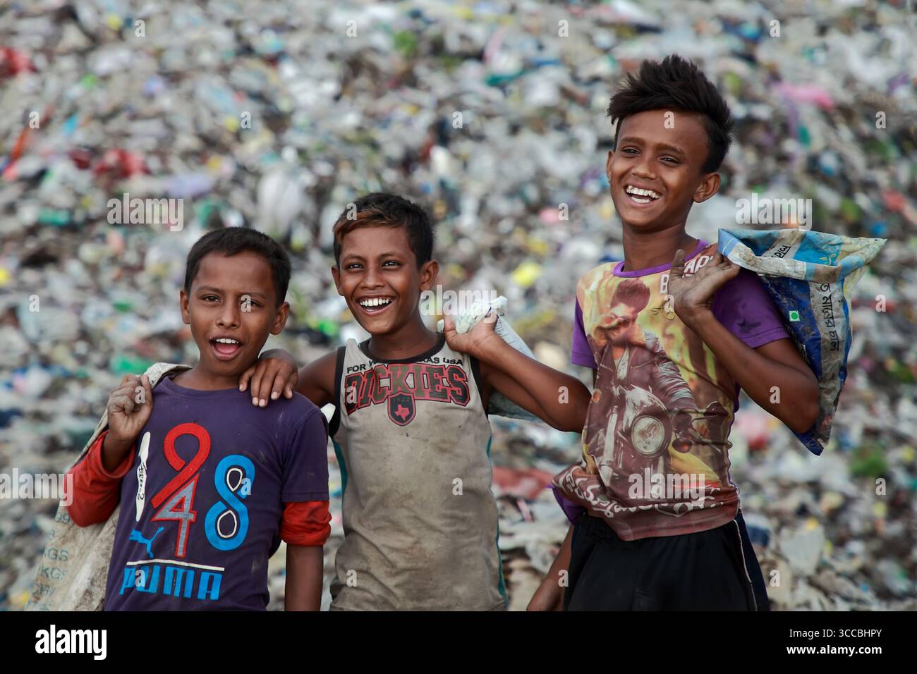 Chattogram, Bangladesh - 05 octobre 2020 : vue de trois garçons souriants debout devant une énorme décharge, leurs visages reflétant la résilience au milieu des énormes déchets. Banque D'Images