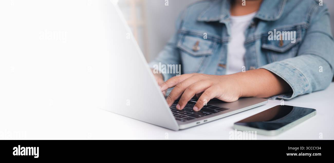 Personne tapant sur ordinateur portable avec smartphone placé sur le bureau, espace de copie à gauche, symbolisant le travail à distance, la communication numérique et l'utilisation de la technologie Banque D'Images