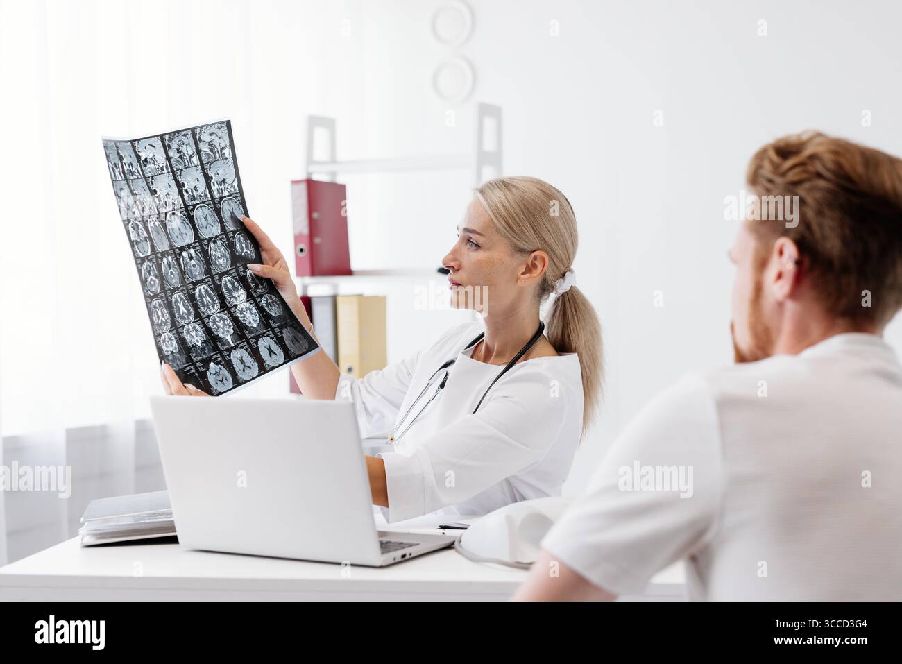 Une femme médecin en manteau blanc explique l'imagerie médicale à un patient masculin dans une clinique moderne, soulignant l'importance de la communication en matière de soins de santé Banque D'Images