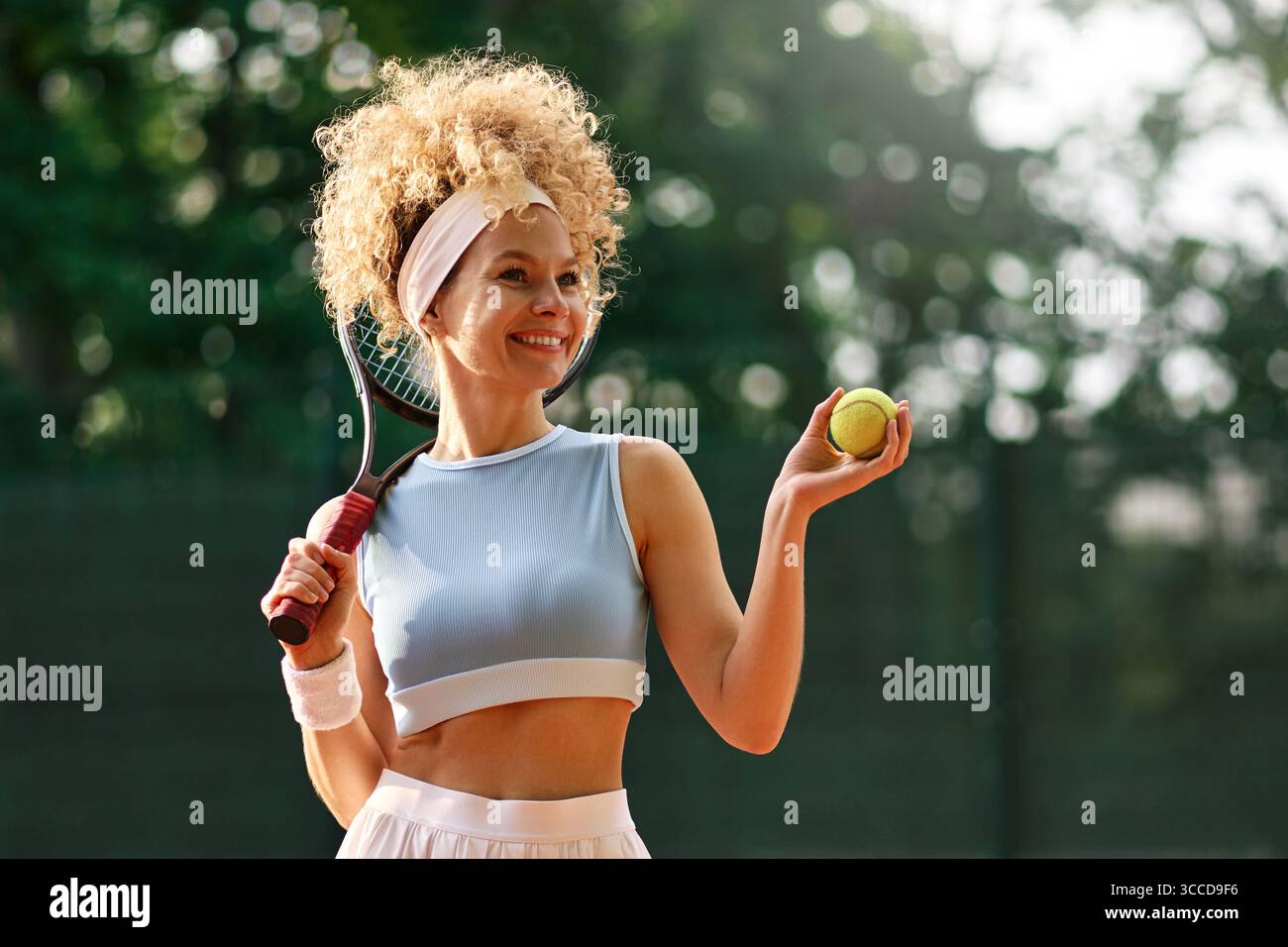 Portrait de femme heureuse avec raquette de tennis et balle sur terrain d'argile, profitant de la pratique estivale. Concept : mode de vie actif, joie du sport, fitness inspirat Banque D'Images