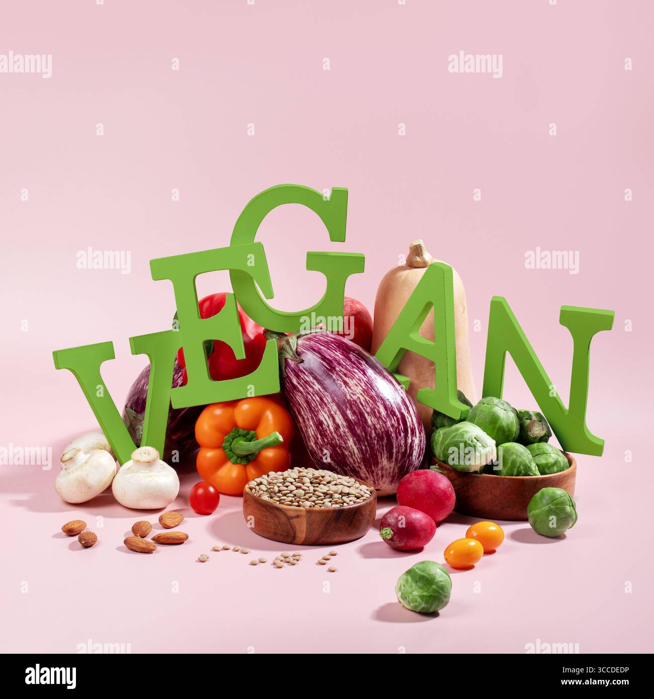 Le mot VEGAN en grandes lettres vertes sur la table rose, entouré de fruits frais, légumes et un bol de lentilles, régime végétalien nature morte Banque D'Images