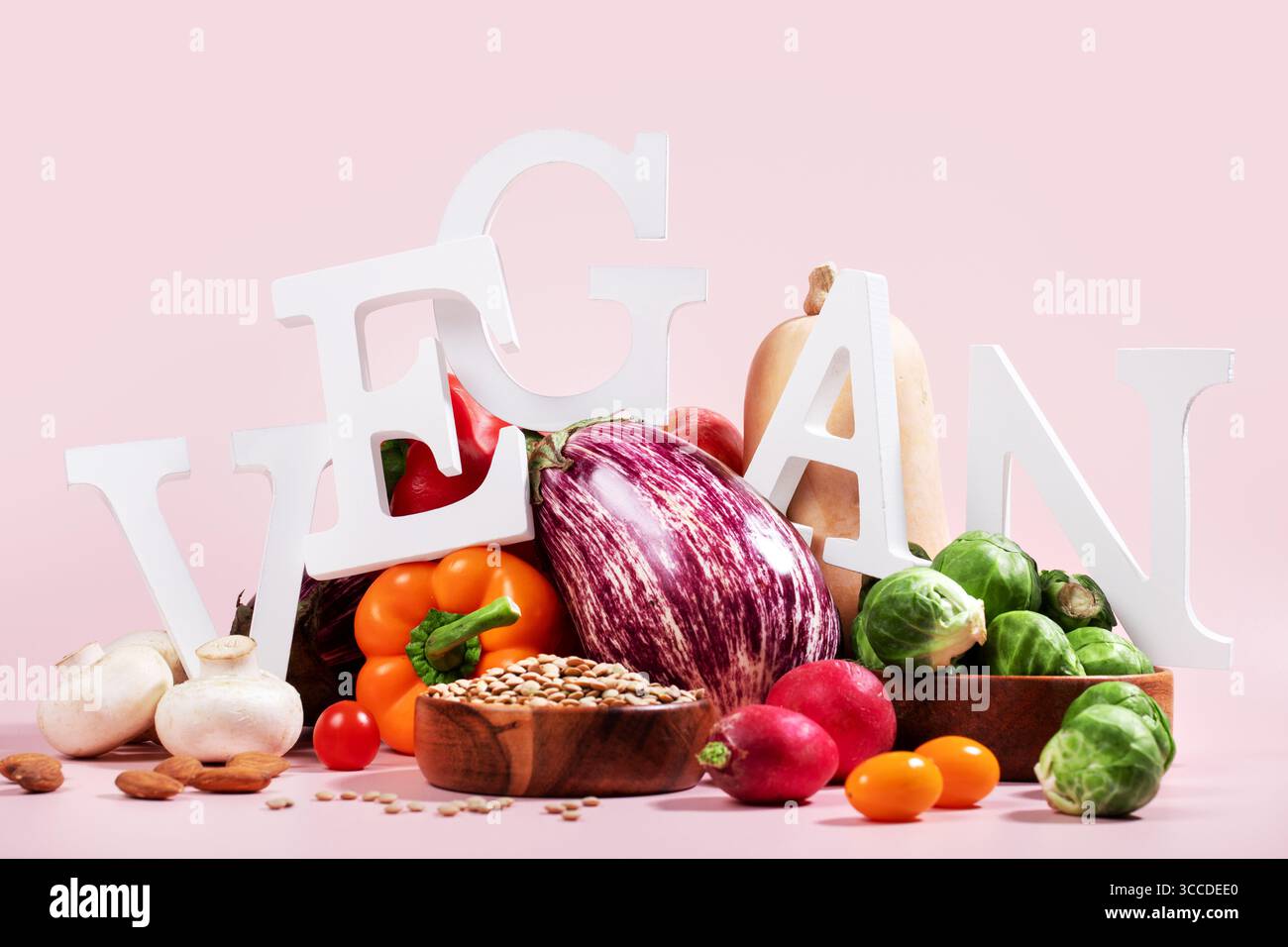 Le mot VEGAN en grandes lettres sur la table rose, entouré de fruits frais, légumes et un bol de lentilles, régime végétalien nature morte Banque D'Images